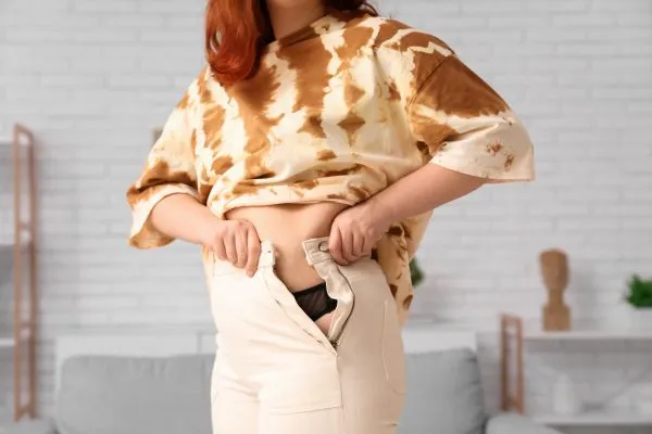 Image of woman trying to do her trousers up after pregnancy weight gain Langside