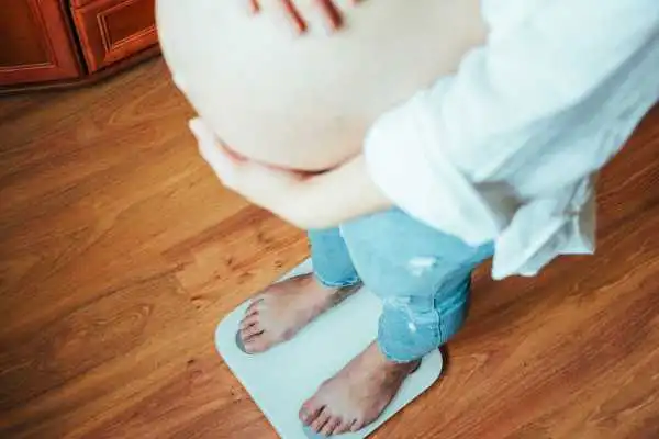 Image of woman weighing herself and experiencing weight gain through pregnancy Langside