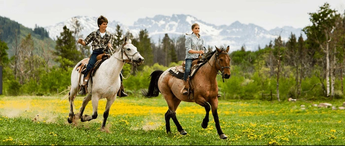 Confident plus-size woman riding Langside a horse through a field with a smile on her face.